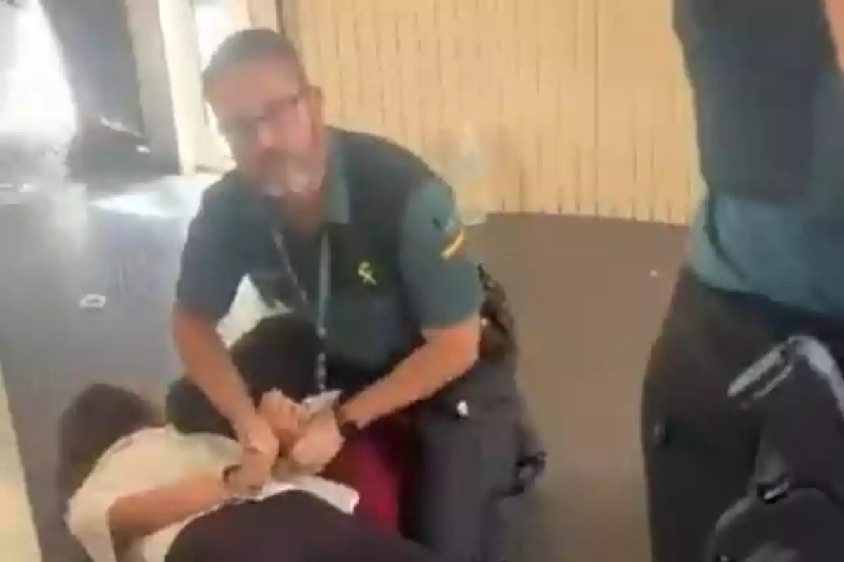 Un agente de policía reduce en el suelo a una persona mientras le coloca esposas en un entorno interior.