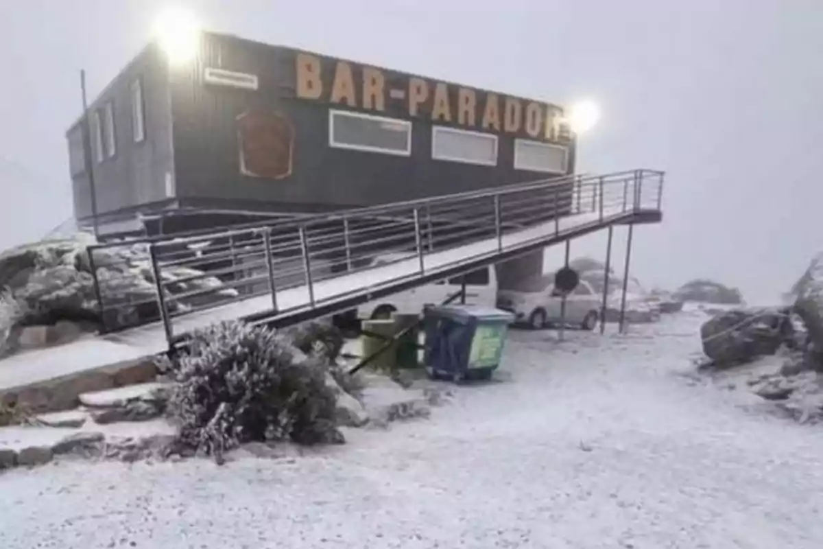 Un bar parador en una zona nevada con una rampa de acceso y algunos autos estacionados alrededor