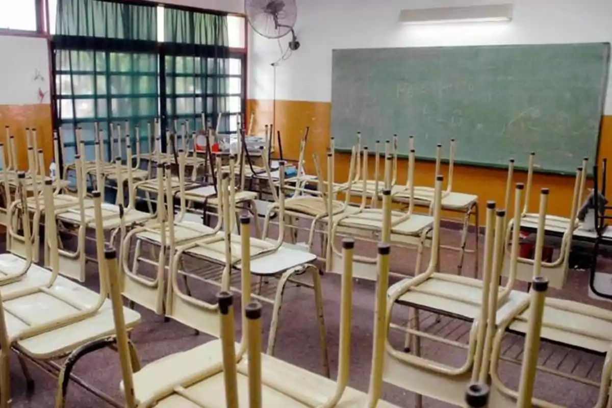 Aula vacía con sillas volteadas sobre los pupitres y un pizarrón al fondo