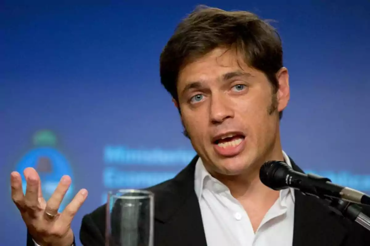 Hombre de cabello castaño hablando frente a un micrófono con fondo azul desenfocado