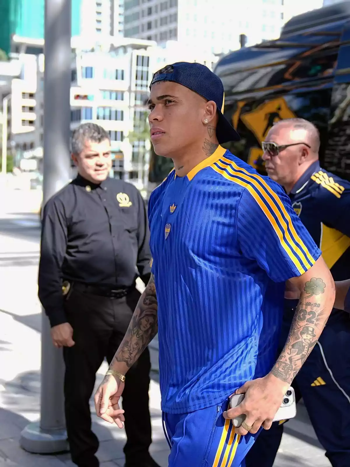 Jugador de fútbol con uniforme azul y amarillo caminando en la calle acompañado de otras personas Jugador de fútbol con uniforme azul y amarillo caminando en la calle acompañado de otras personas