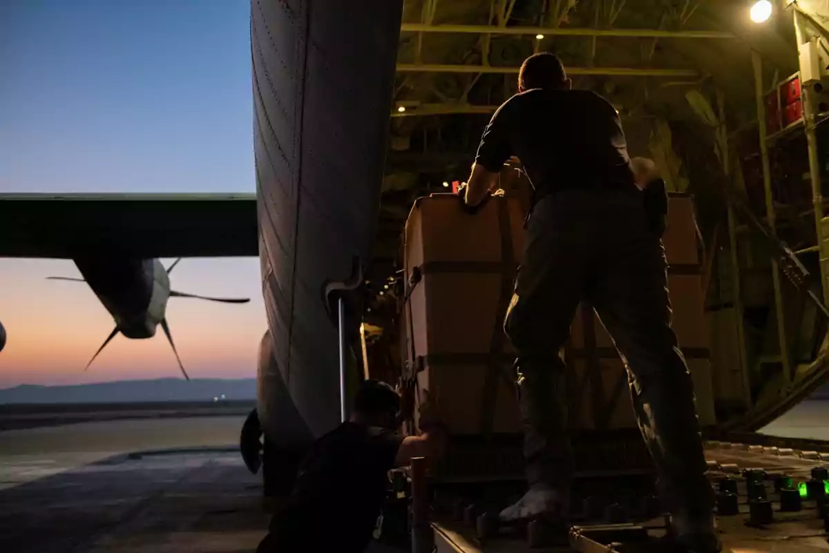 Dos personas cargan una gran caja dentro de un avión de carga al atardecer