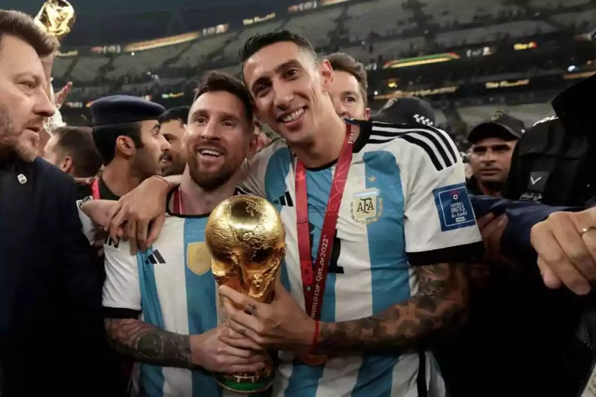 Two Argentine players smile and celebrate, hugging each other while holding the World Cup trophy in a crowded stadium. Two Argentine players smile and celebrate, hugging each other while holding the World Cup trophy in a crowded stadium.