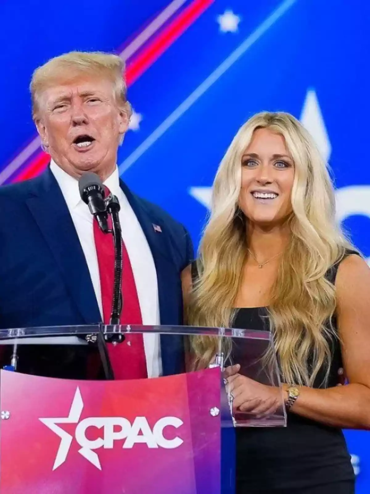Two people standing behind a podium with the CPAC logo against a blue background with stars Two people standing behind a podium with the CPAC logo against a blue background with stars