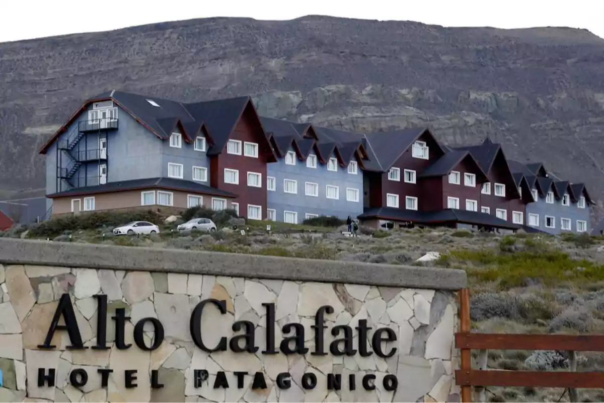 Fachada del hotel Alto Calafate en la Patagonia con un cartel de piedra en primer plano y montañas al fondo Fachada del hotel Alto Calafate en la Patagonia con un cartel de piedra en primer plano y montañas al fondo