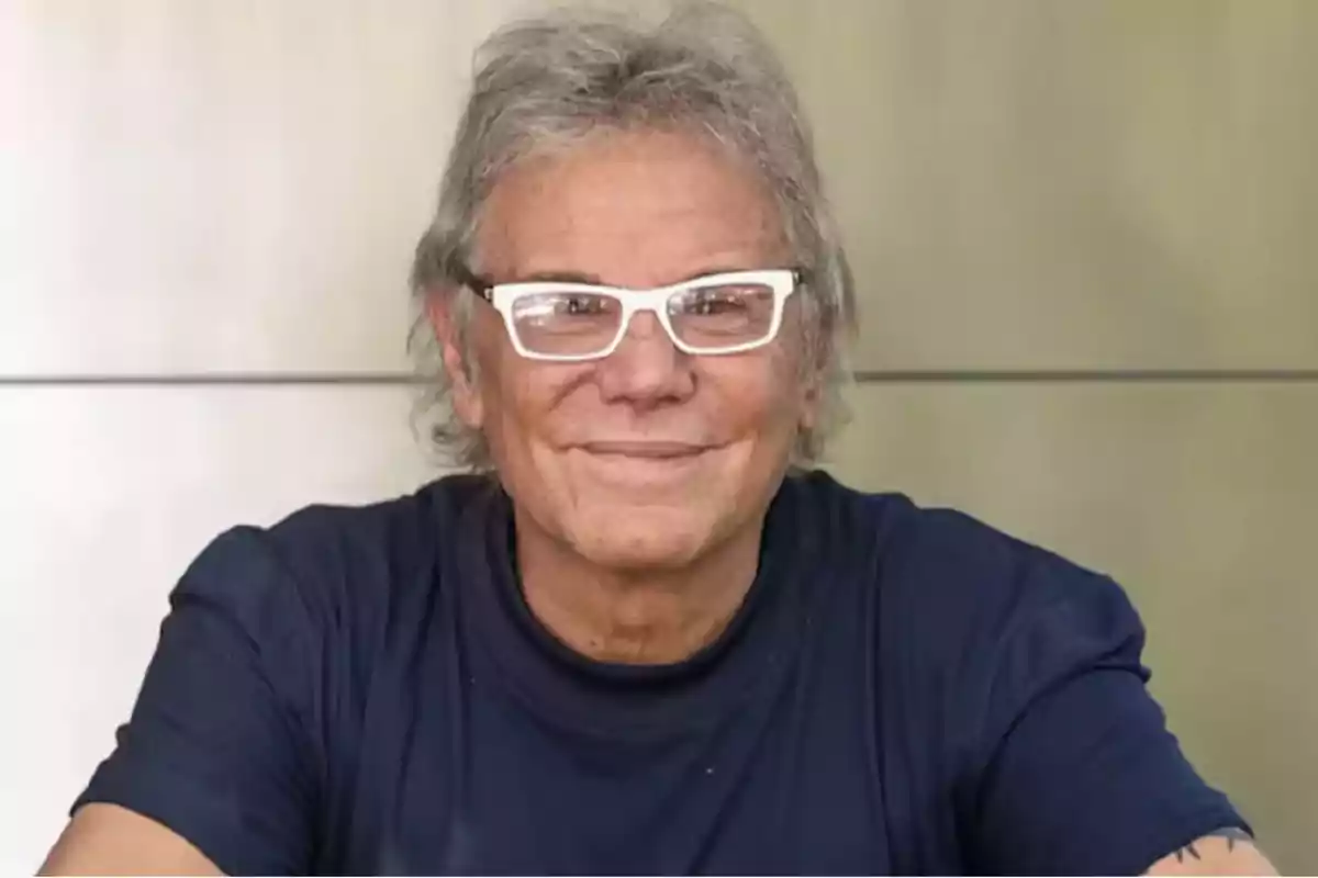 Gray-haired man with white glasses smiling and wearing a dark blue t-jersey