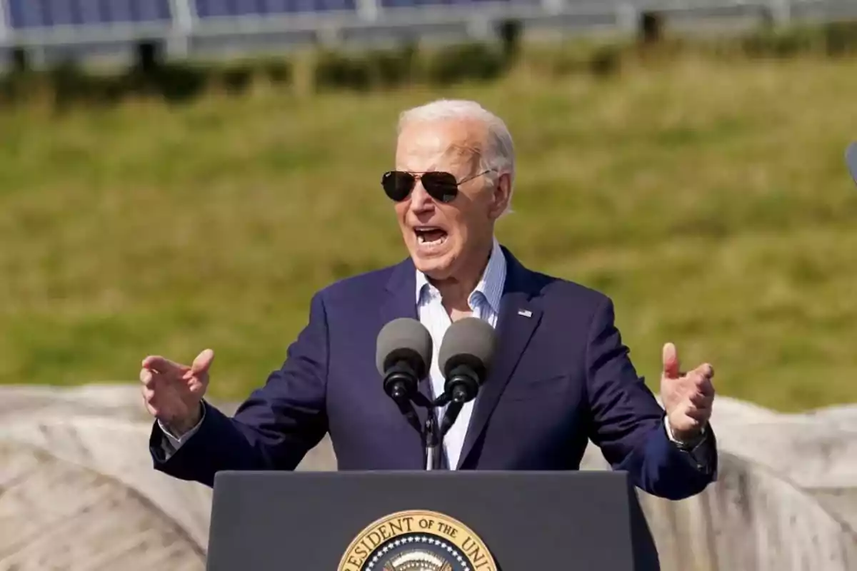 Gray-haired man with sunglasses speaking at an outdoor podium