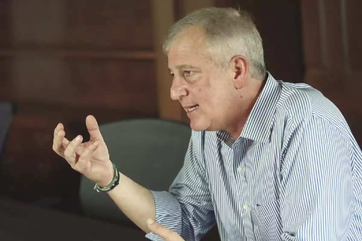Gray-haired man in a striped jersey speaking and gesturing with his hand in an office Gray-haired man in a striped jersey speaking and gesturing with his hand in an office