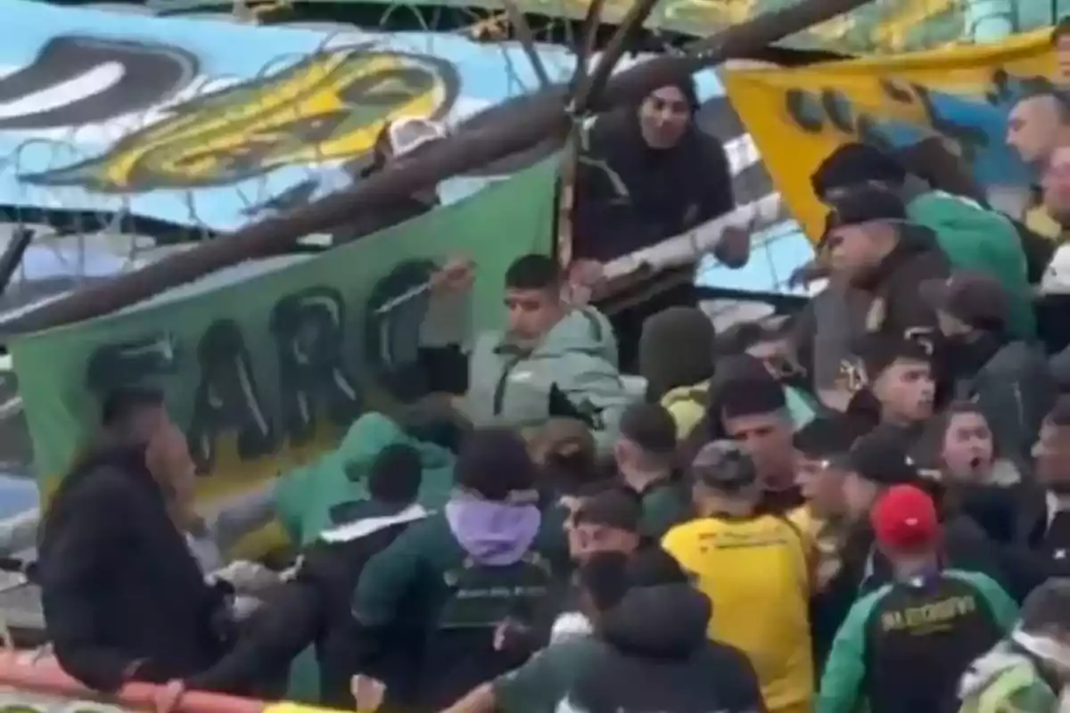 Aficionados de fútbol discutiendo y empujándose en una tribuna llena, con banderas y pancartas de colores verde y amarillo al fondo Aficionados de fútbol discutiendo y empujándose en una tribuna llena, con banderas y pancartas de colores verde y amarillo al fondo