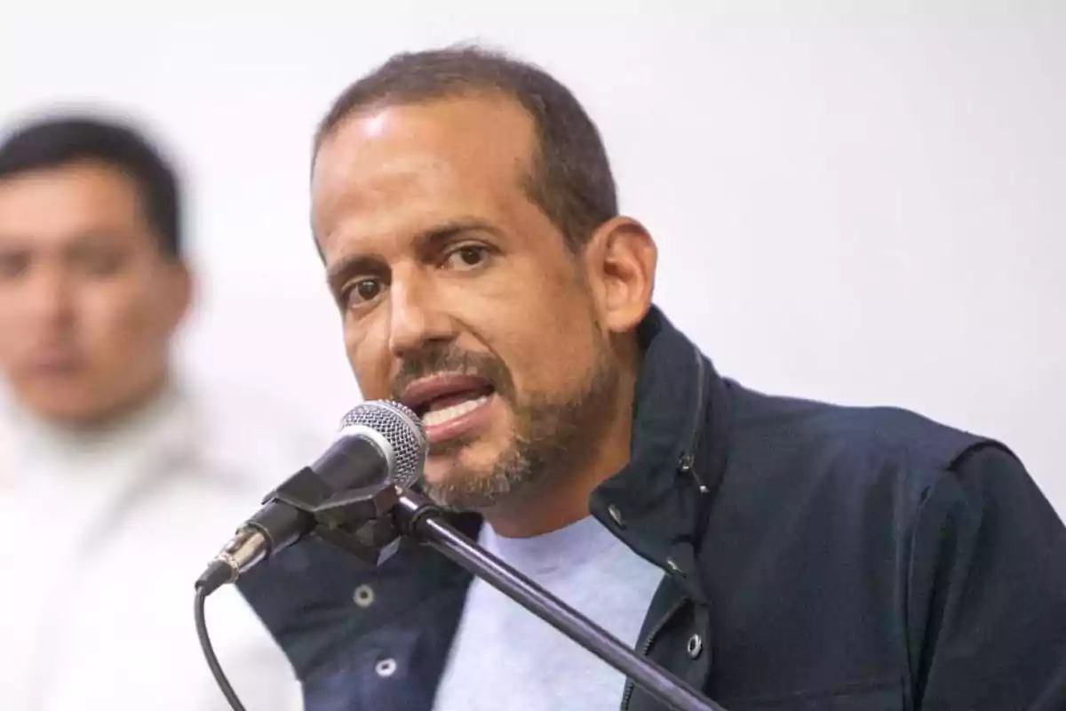Short-haired, bearded man speaking in front of a microphone with a blurred background