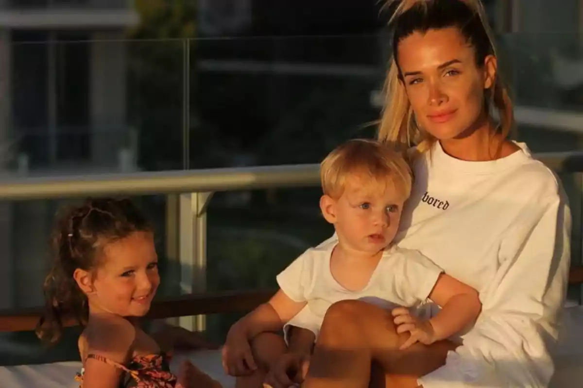 Una mujer joven sentada al aire libre con dos niños pequeños disfrutando de la luz del atardecer Una mujer joven sentada al aire libre con dos niños pequeños disfrutando de la luz del atardecer