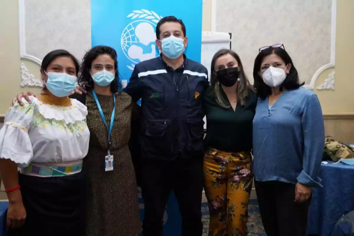 Cinco personas con cubrebocas posan juntas frente a un cartel azul de UNICEF en un ambiente interior.