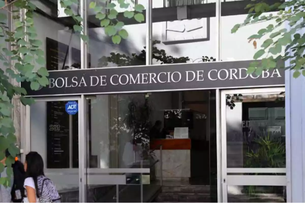 Main entrance of the Córdoba Stock Exchange with people entering and vegetation in the foreground Main entrance of the Córdoba Stock Exchange with people entering and vegetation in the foreground