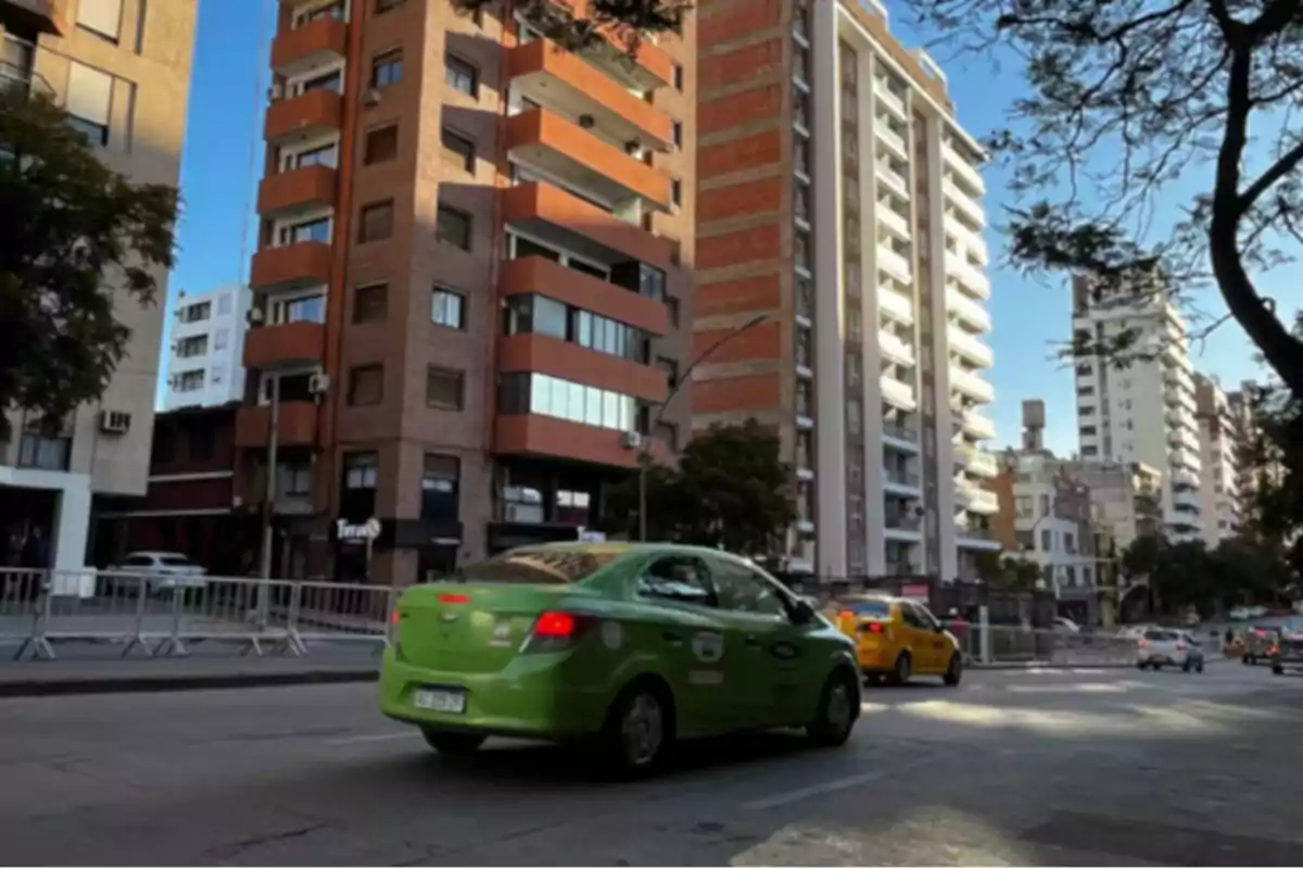 A green taxi drives down an avenue surrounded by tall buildings in a city during the day.