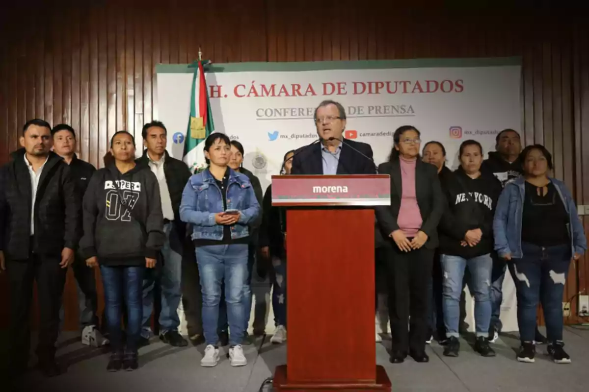A group of people is gathered at a press conference in the Chamber of Deputies, with a man speaking at a podium that has the Morena logo and a Mexican flag in the background.