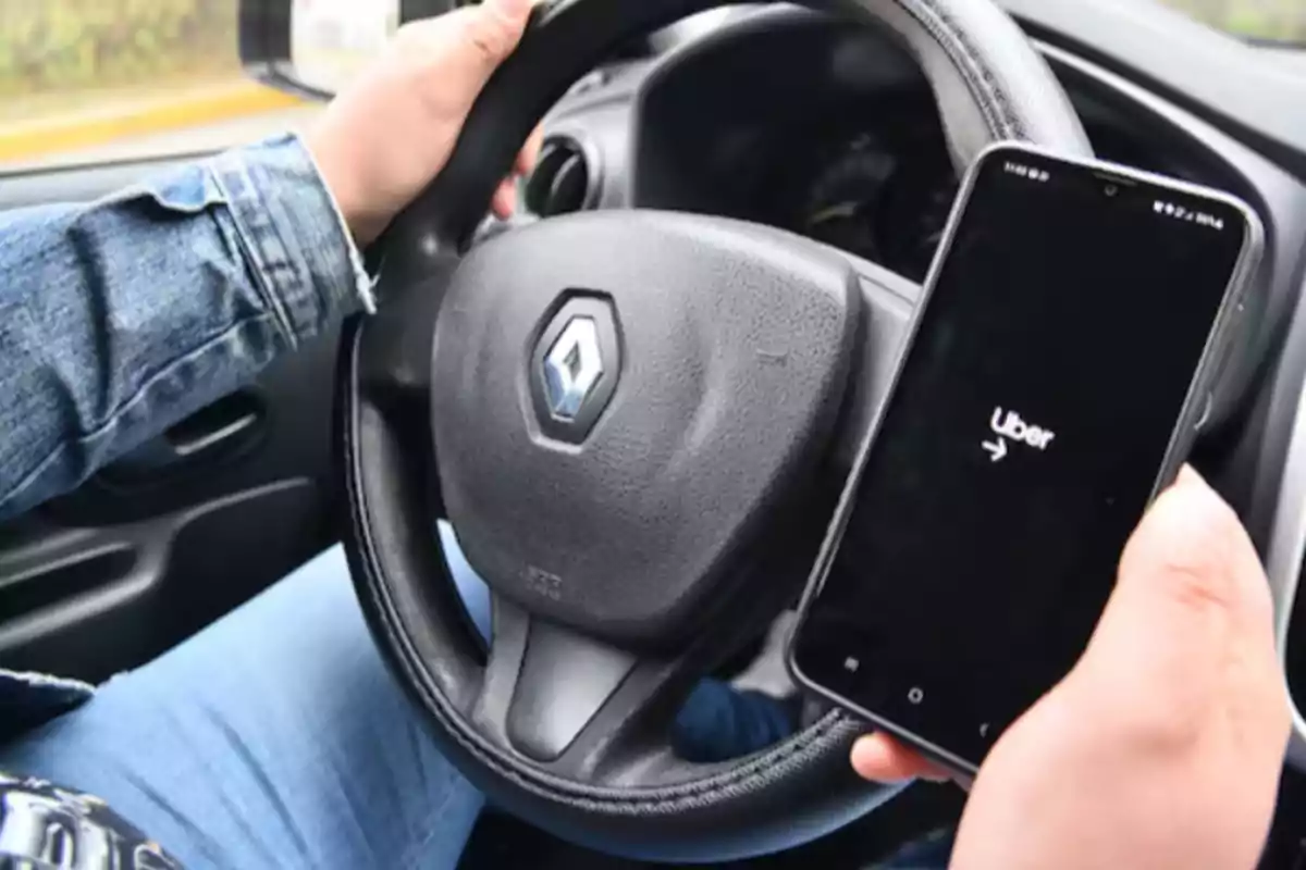 Persona conduciendo un auto Renault mientras sostiene un teléfono móvil con la aplicación de Uber abierta