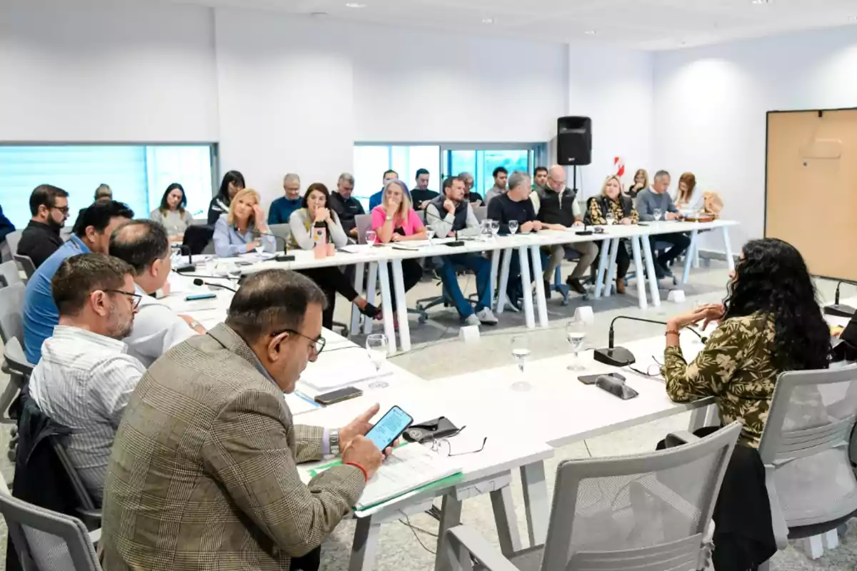 Personas sentadas alrededor de varias mesas blancas en una sala de reuniones participando en una discusión grupal