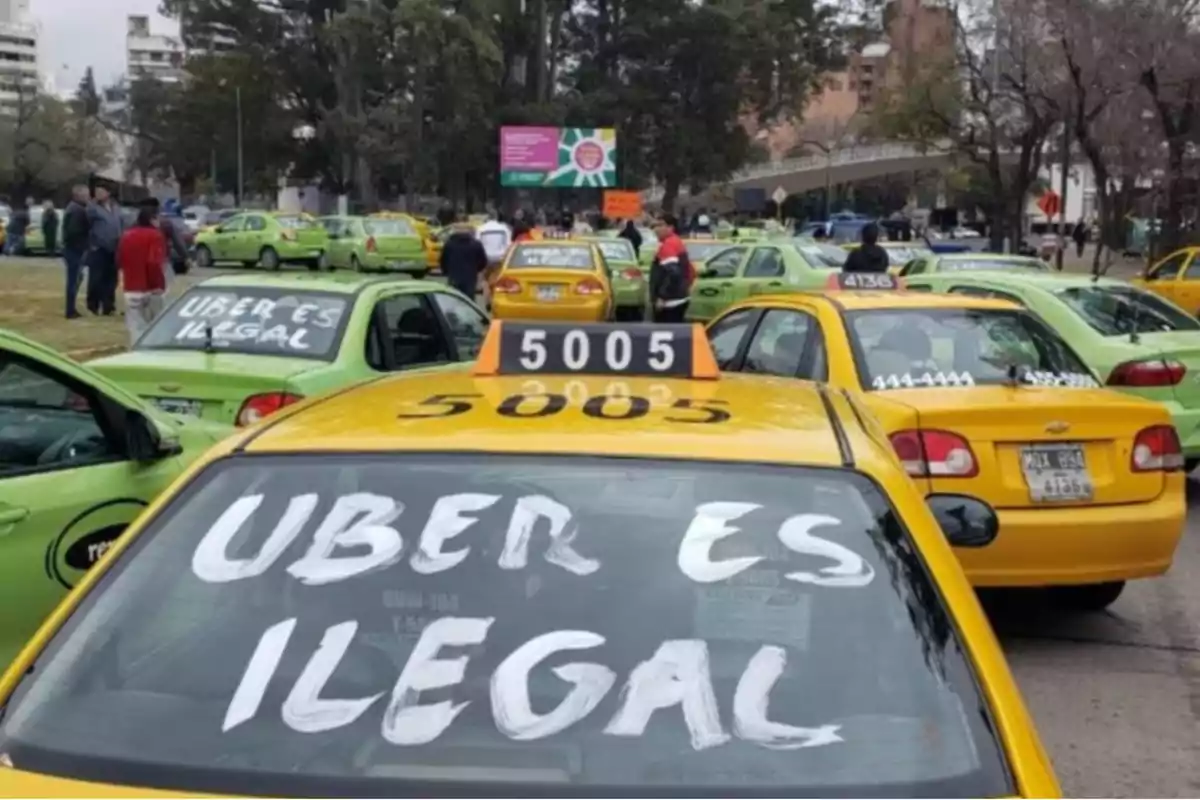 Taxis amarillos y verdes estacionados con mensajes en los parabrisas que dicen Uber es ilegal durante una protesta en la vía pública
