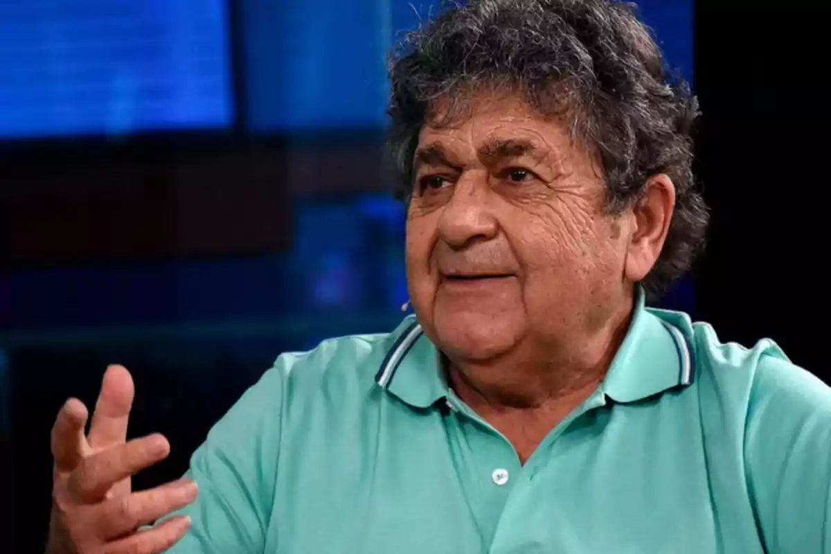 Gray-haired, curly-haired man in a light green polo jersey gesturing while speaking in a television studio Gray-haired, curly-haired man in a light green polo jersey gesturing while speaking in a television studio