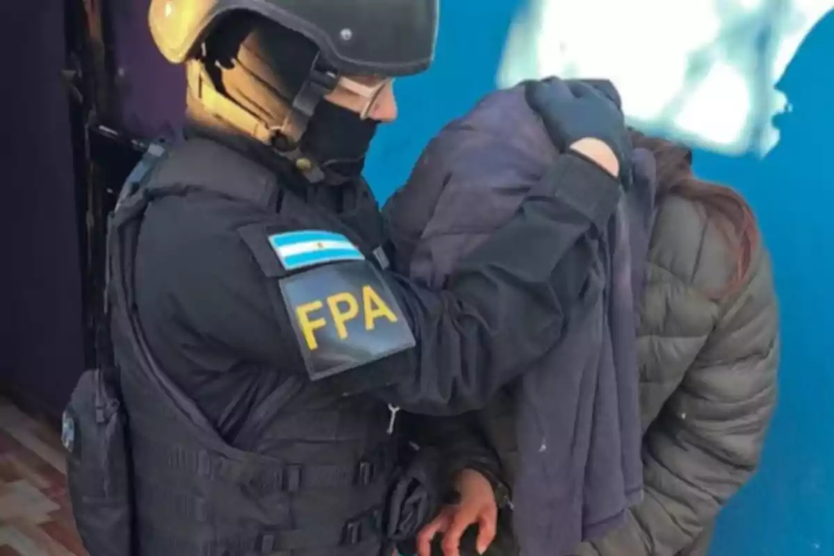 Agente de la FPA deteniendo a una persona con la cabeza cubierta frente a una pared azul