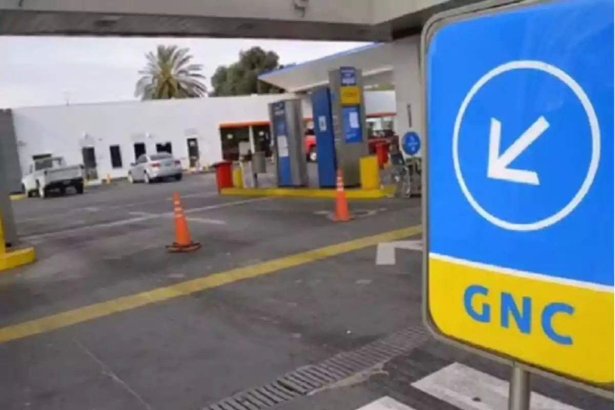 Blue and yellow GNC sign at a gas station with cars and orange cones