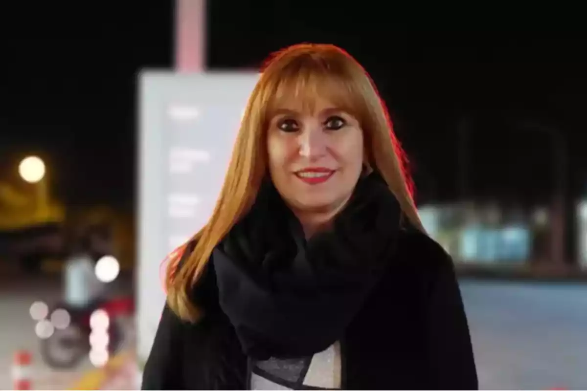 Mujer de cabello largo y pelirrojo con bufanda negra sonriendo al aire libre durante la noche