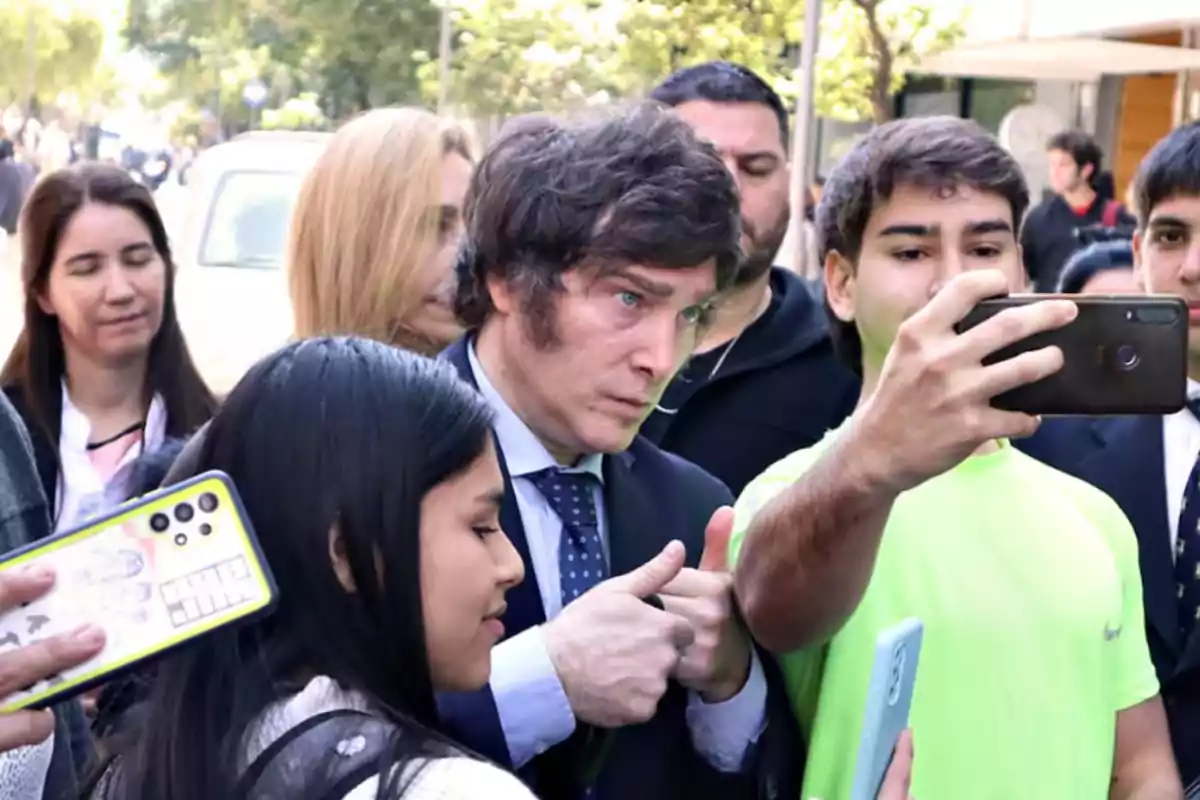 Un grupo de personas se toma una selfie en la calle mientras un hombre de traje hace el gesto de pulgares arriba