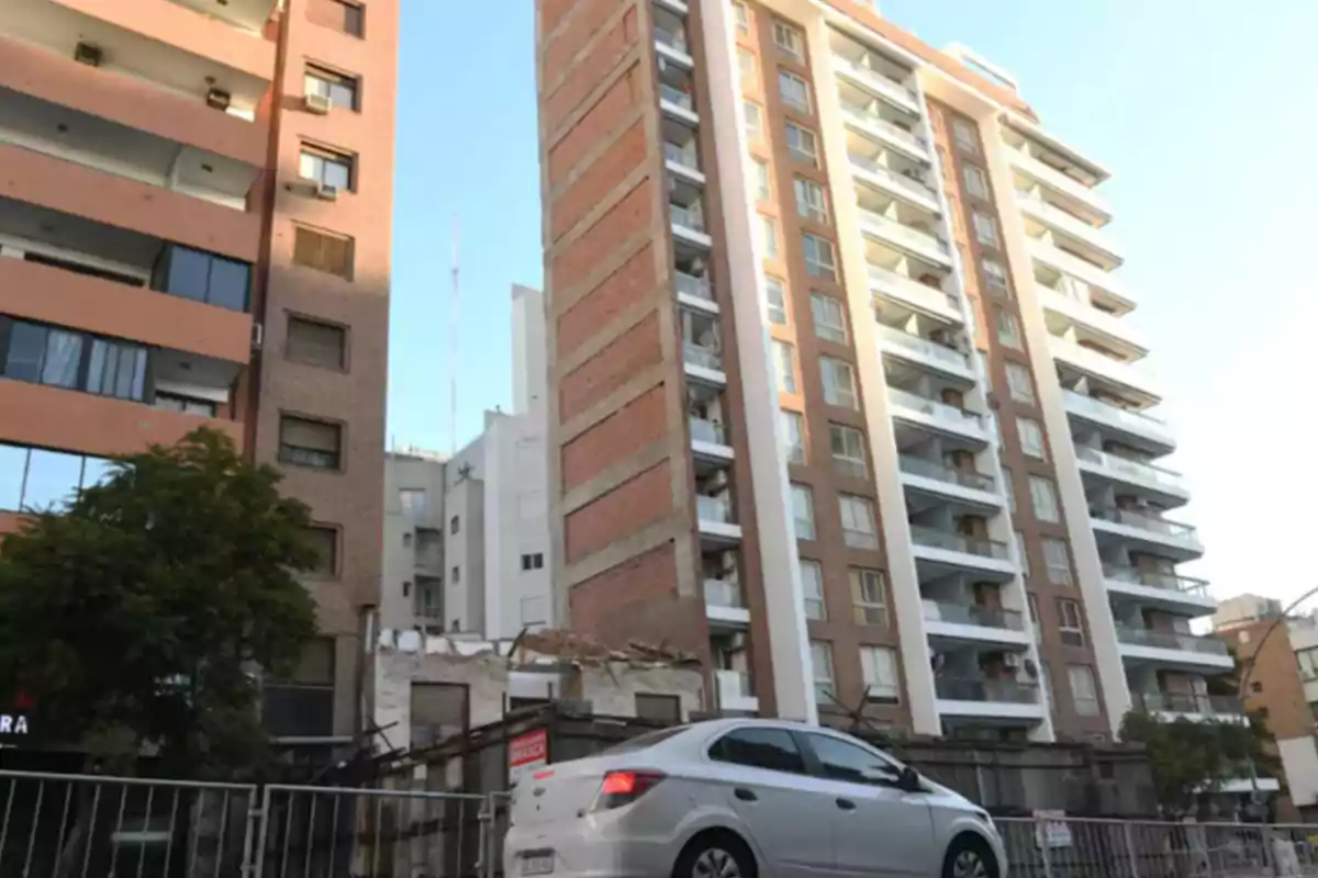 Edificio de departamentos de varios pisos con balcones y un auto plateado estacionado al frente en una calle urbana Edificio de departamentos de varios pisos con balcones y un auto plateado estacionado al frente en una calle urbana