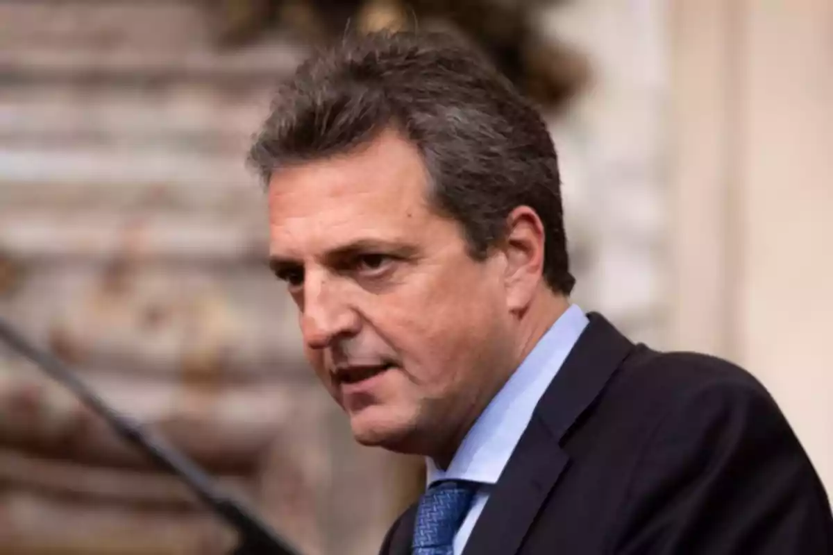 Hombre de cabello corto y canoso vistiendo traje oscuro y corbata azul en un entorno formal