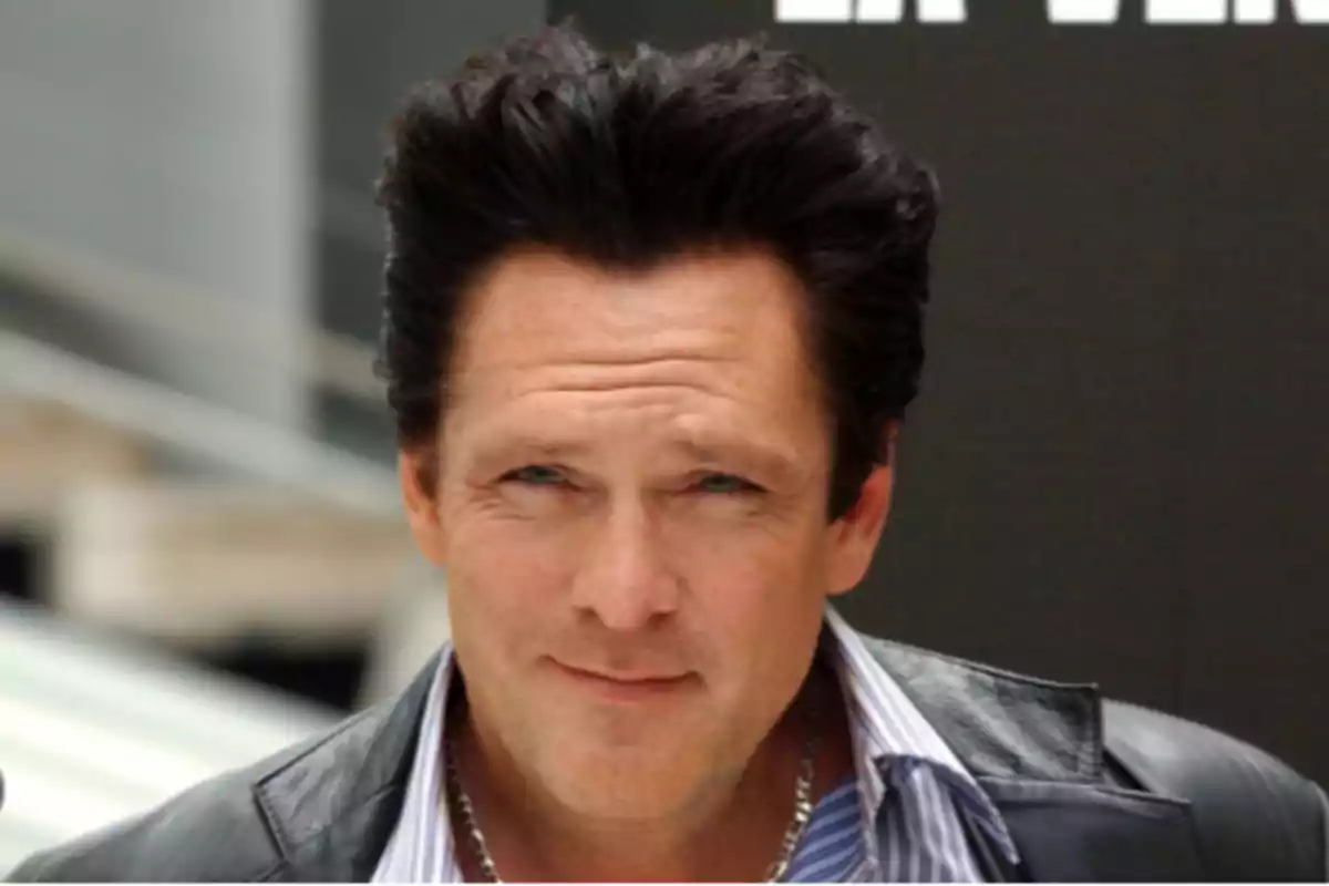Dark-haired man with his hair styled up, wearing a leather jacket and a striped jersey, looking at the camera