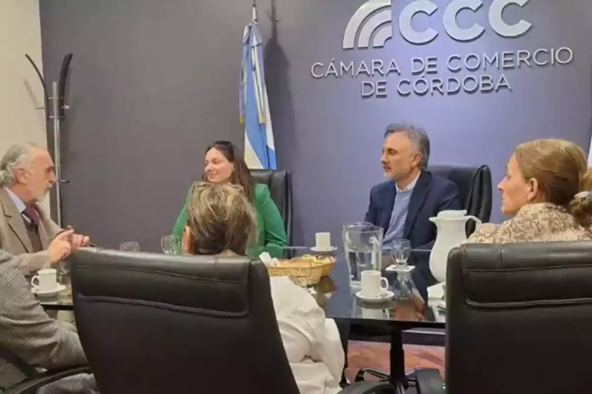 Five people sitting around a meeting table in an office of the Córdoba Chamber of Commerce with an Argentine flag in the background and coffee cups on the table Five people sitting around a meeting table in an office of the Córdoba Chamber of Commerce with an Argentine flag in the background and coffee cups on the table