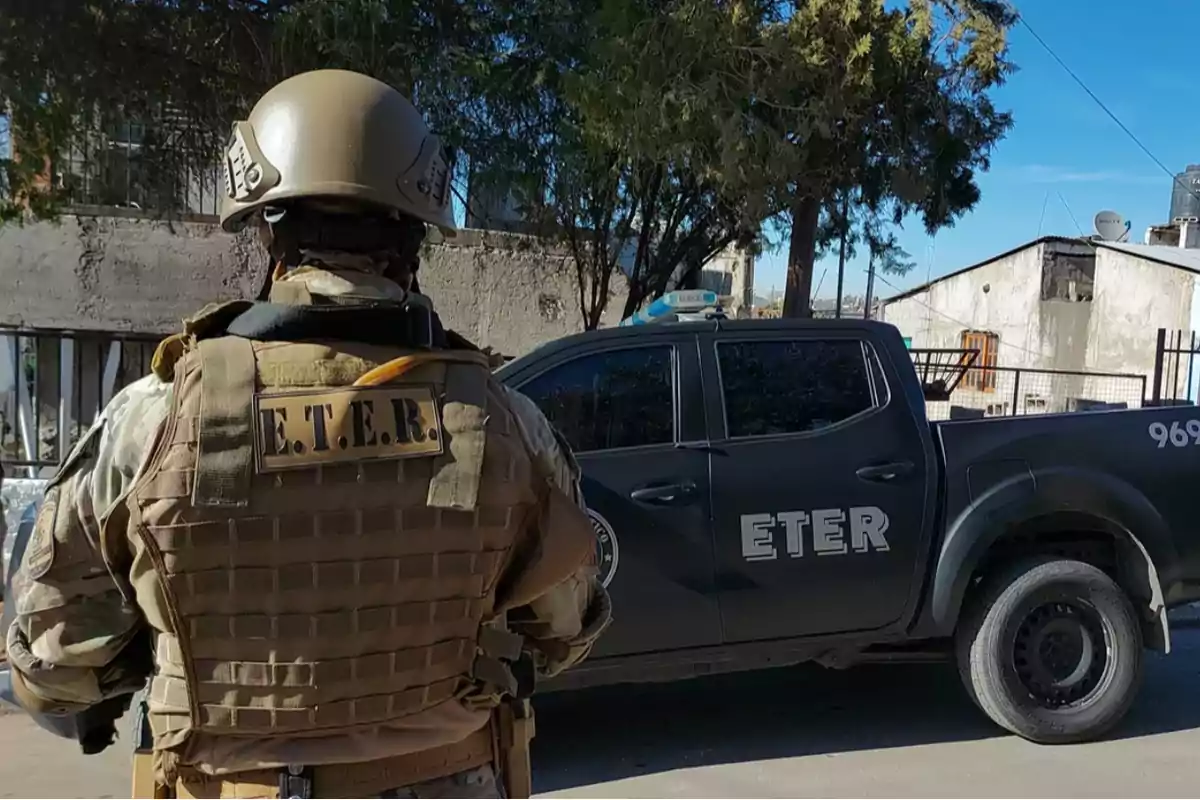 Agente de ETER con chaleco antibalas y casco de espaldas junto a una camioneta policial negra en una calle urbana