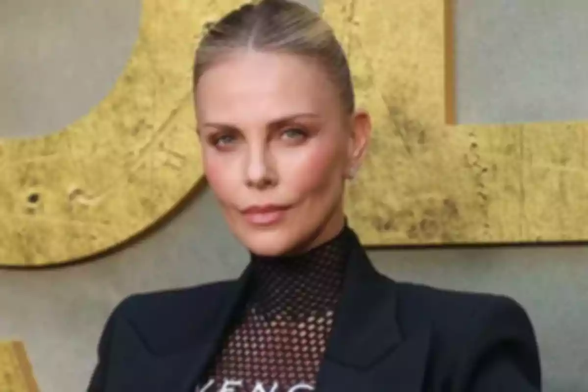 Blonde woman with her hair up wearing a black blazer and a black mesh blouse posing in front of a gold background Blonde woman with her hair up wearing a black blazer and a black mesh blouse posing in front of a gold background