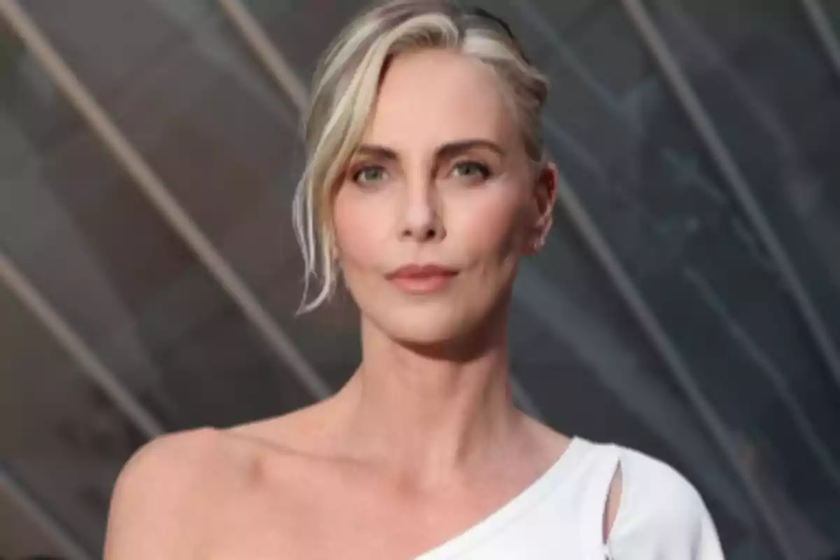 Blonde woman with her hair up and a white dress posing in front of a dark geometric background