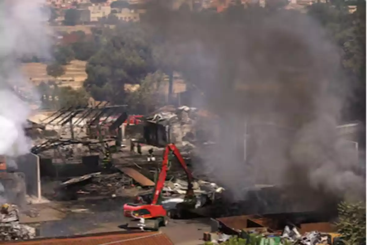 Fire in an industrial area with heavy machinery and columns of black smoke rising into the sky