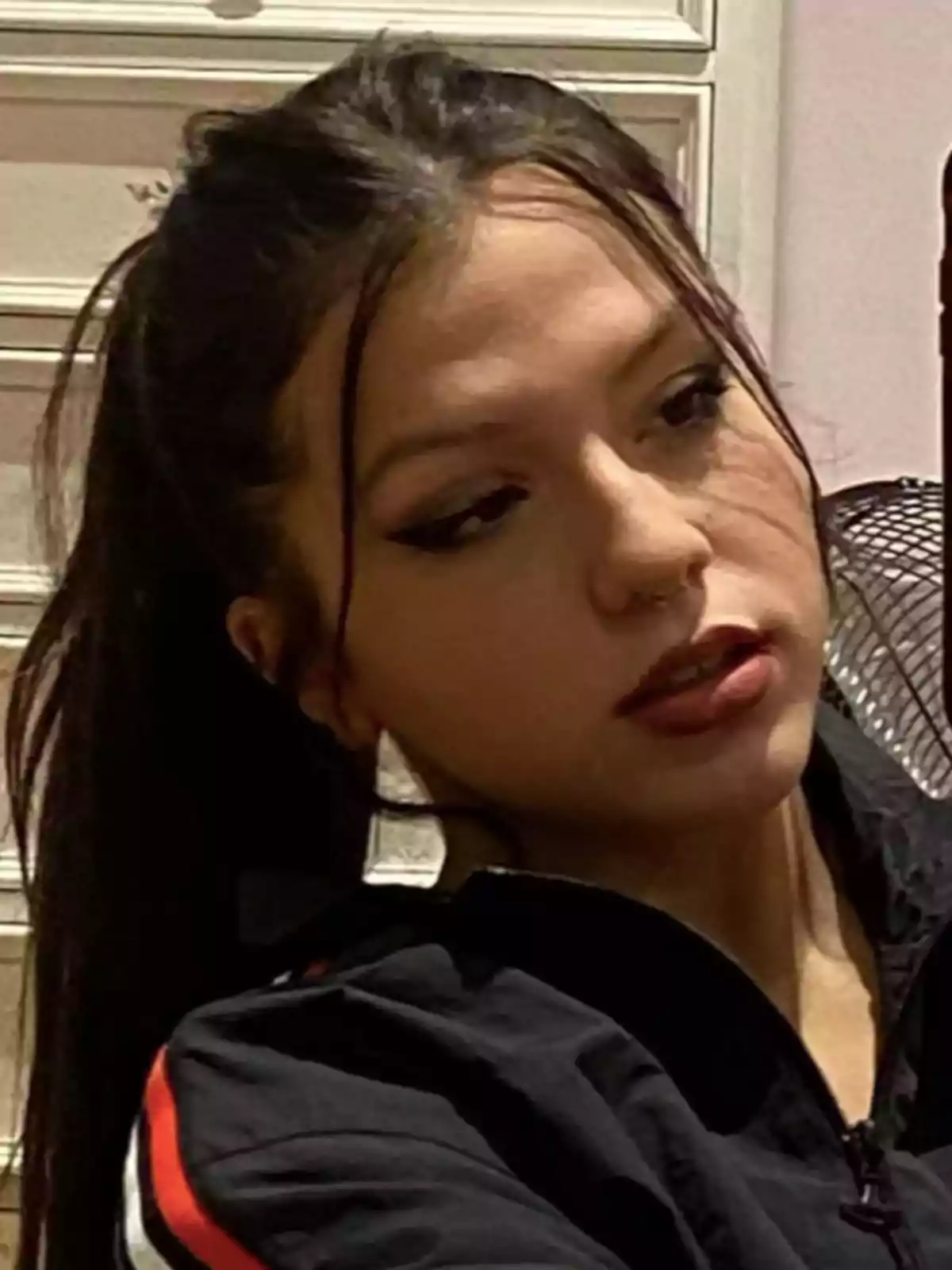 Young woman with dark hair tied back and bold makeup, wearing a black jacket with red and white details Young woman with dark hair tied back and bold makeup, wearing a black jacket with red and white details