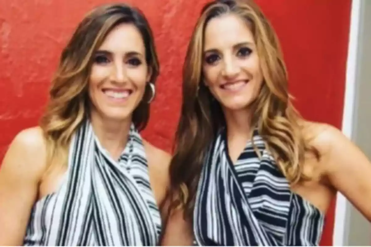 Two smiling women with long, loose hair, both wearing black and white striped blouses, pose together in front of a red wall. Two smiling women with long, loose hair, both wearing black and white striped blouses, pose together in front of a red wall.