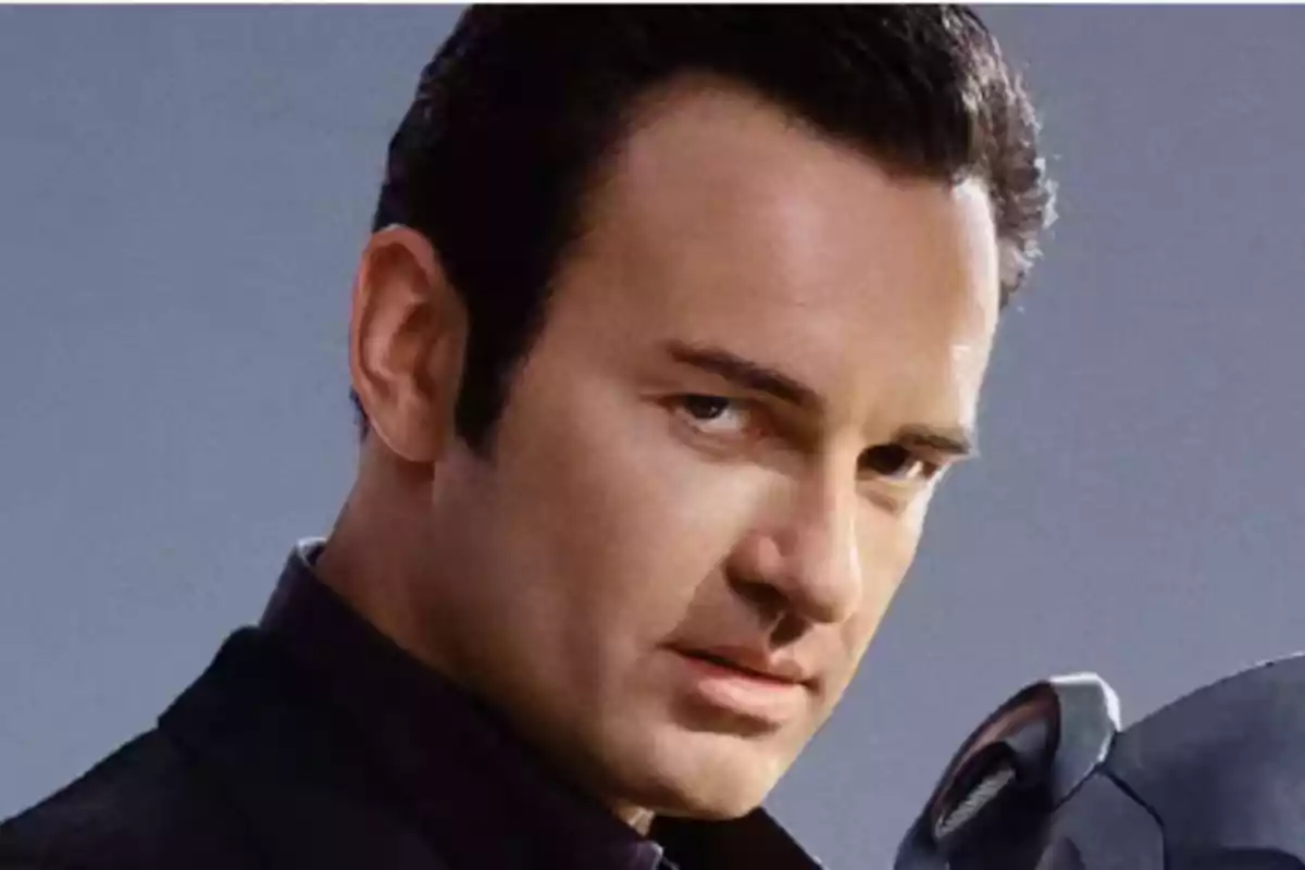 Dark-haired man with a serious expression looking forward and a gray background