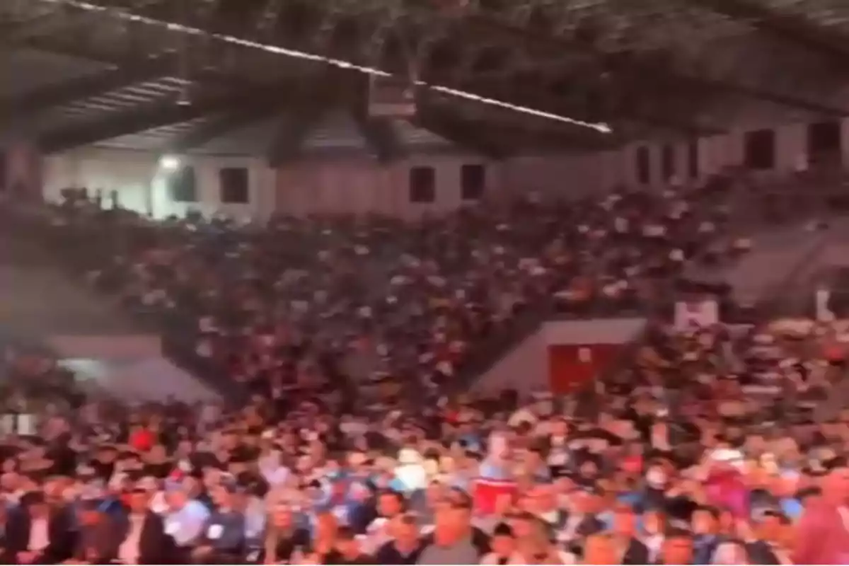 Auditorio techado lleno de personas sentadas en las gradas y en la parte baja, con ambiente de evento masivo.