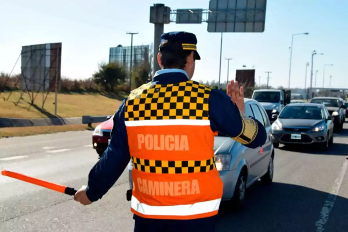 A highway patrol officer stops traffic on a road while holding an orange signaling baton. A highway patrol officer stops traffic on a road while holding an orange signaling baton.