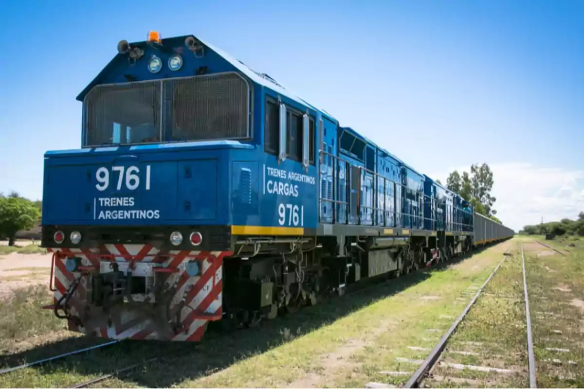 Blue freight train from Trenes Argentinos running on a track in a rural area under a clear sky Blue freight train from Trenes Argentinos running on a track in a rural area under a clear sky