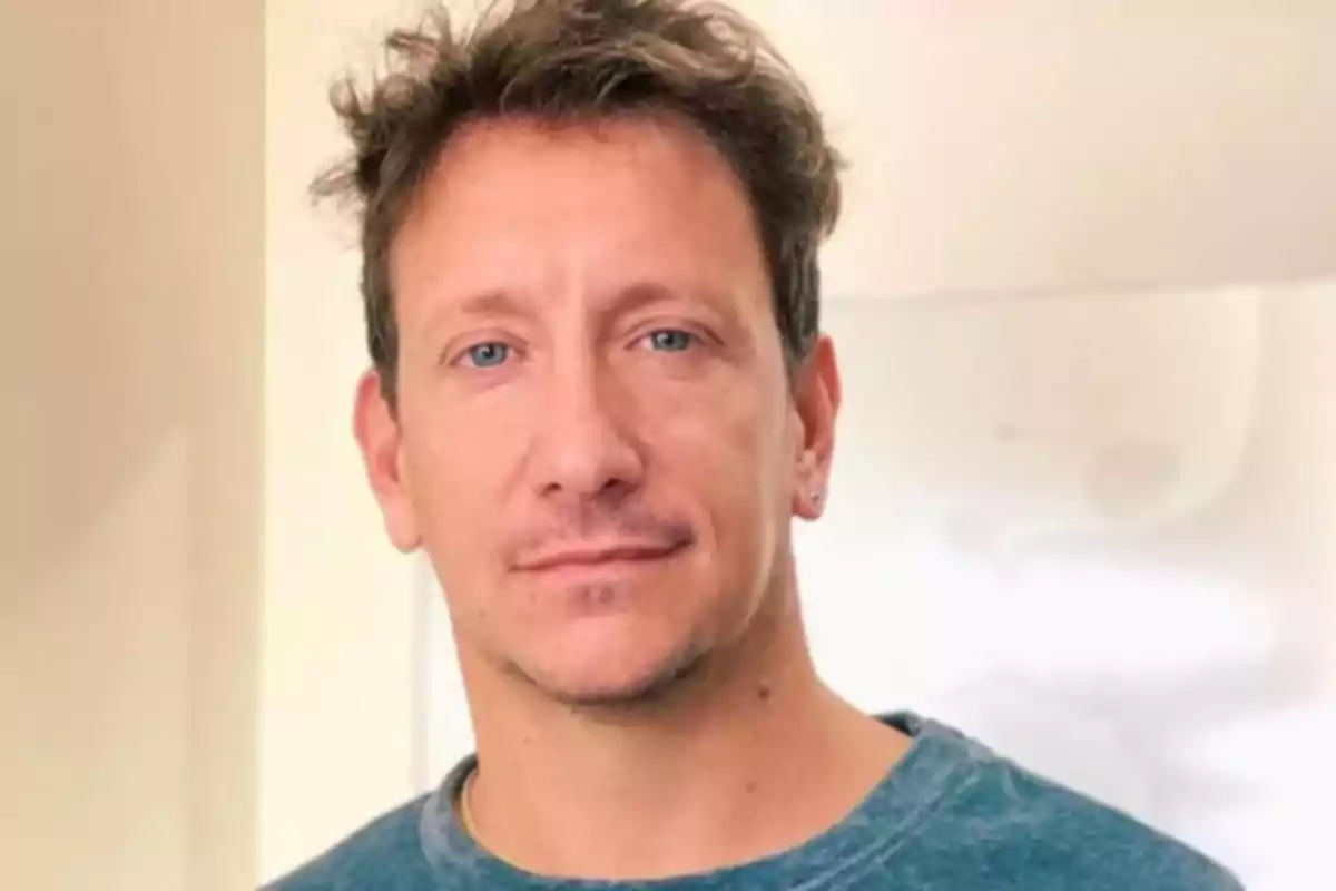 Hombre de cabello corto y despeinado con camiseta azul mirando a la cámara en un entorno interior iluminado