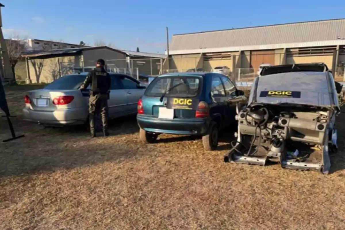 Three cars parked on a lot, one of them dismantled, with DGIC signs and a uniformed person inspecting one of the vehicles. Three cars parked on a lot, one of them dismantled, with DGIC signs and a uniformed person inspecting one of the vehicles.