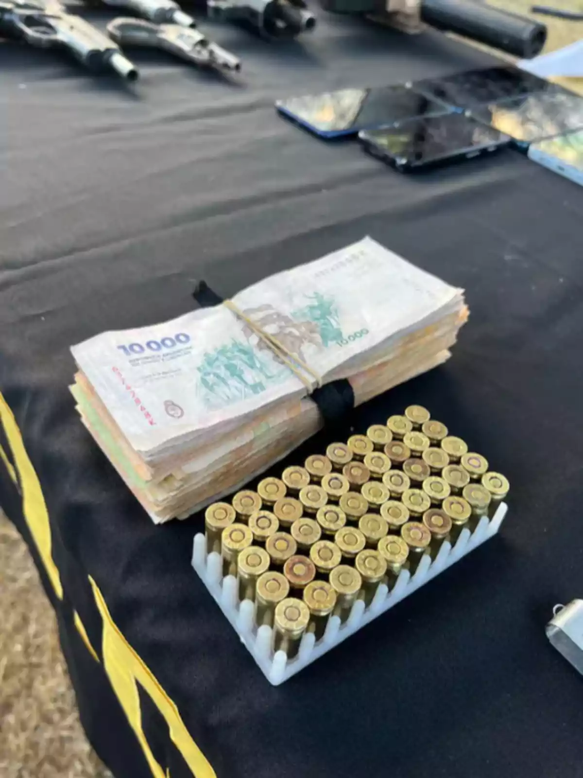 High-denomination bill, bullet cartridges, and various objects on a black table High-denomination bill, bullet cartridges, and various objects on a black table