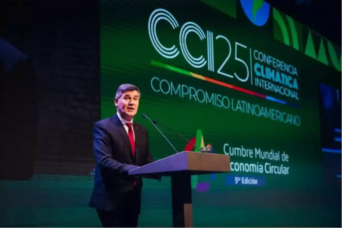 Hombre de traje hablando en un podio durante una conferencia climática internacional con una pantalla verde de fondo que muestra el texto Compromiso Latinoamericano y Cumbre Mundial de Economía Circular