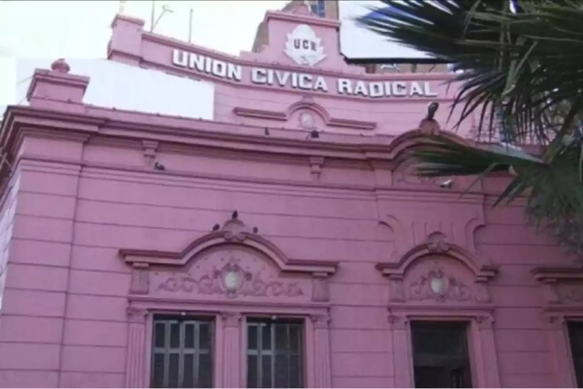 Fachada de un edificio antiguo pintado de rosa con un cartel que dice Union Civica Radical y una palmera en primer plano Fachada de un edificio antiguo pintado de rosa con un cartel que dice Union Civica Radical y una palmera en primer plano