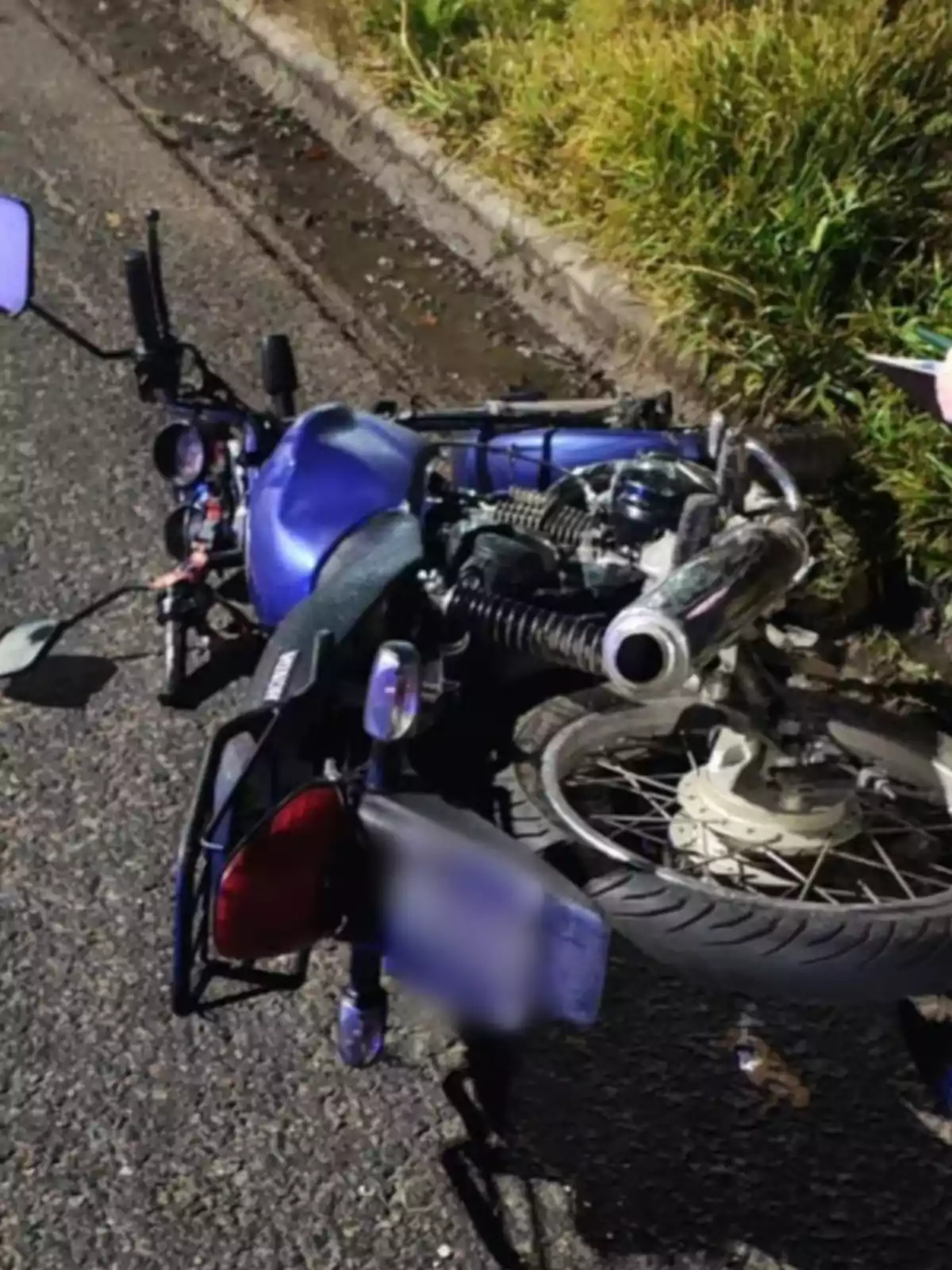 Motocicleta azul tirada de lado sobre el asfalto junto a la banqueta y pasto Motocicleta azul tirada de lado sobre el asfalto junto a la banqueta y pasto