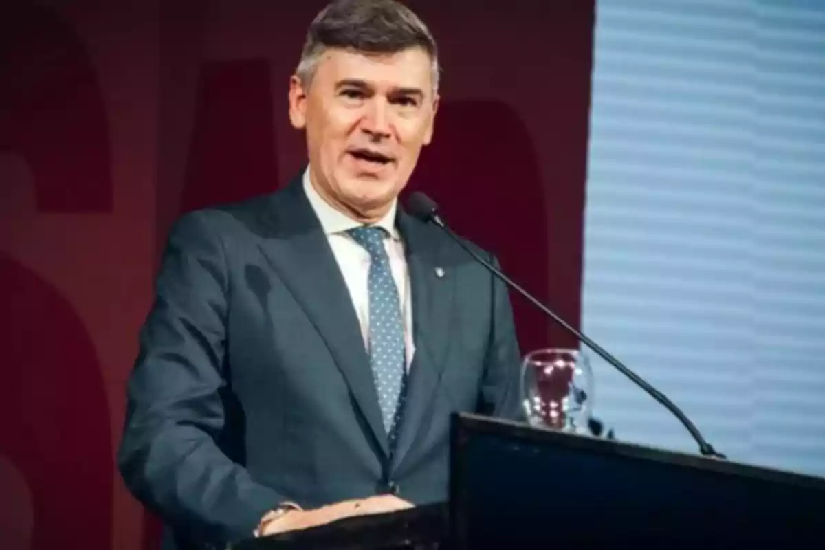 Hombre de traje azul hablando en un podio con micrófono y fondo rojo Hombre de traje azul hablando en un podio con micrófono y fondo rojo