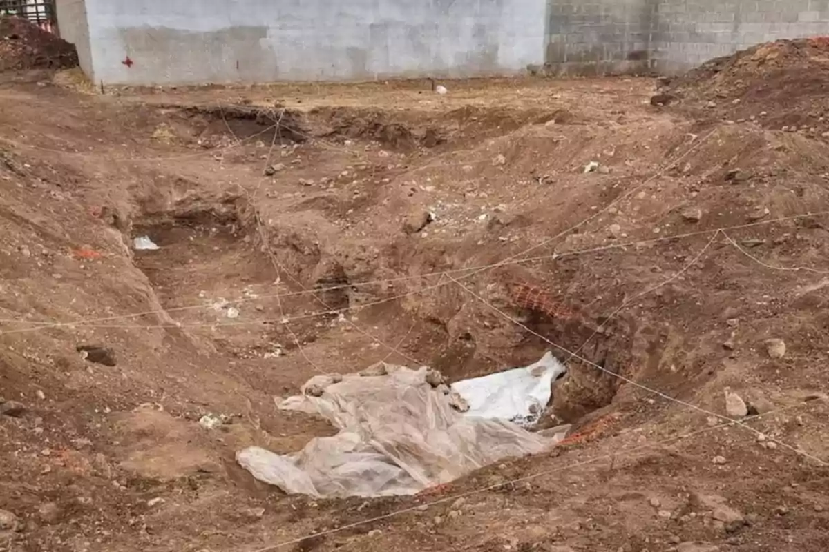 Excavation in soil with plastic sheets covering part of it and ropes marking off the area