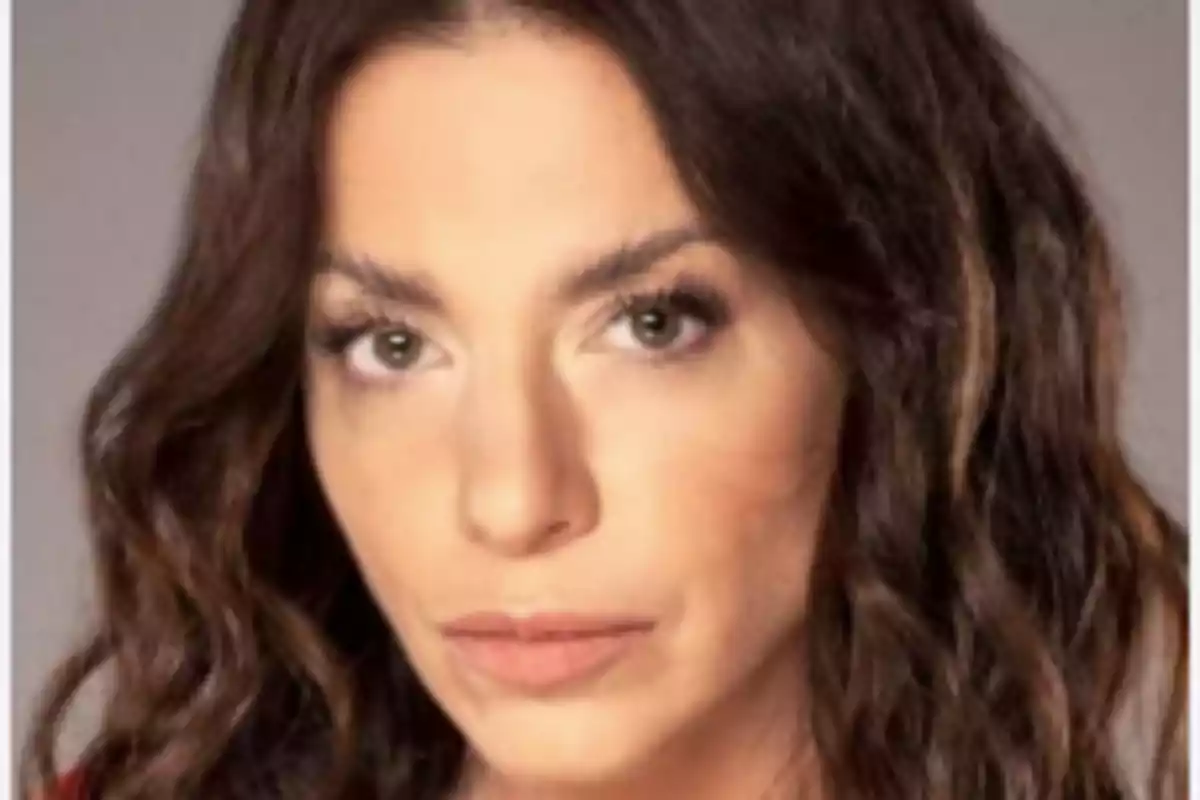Mujer de cabello castaño ondulado y largo con expresión seria mirando al frente
